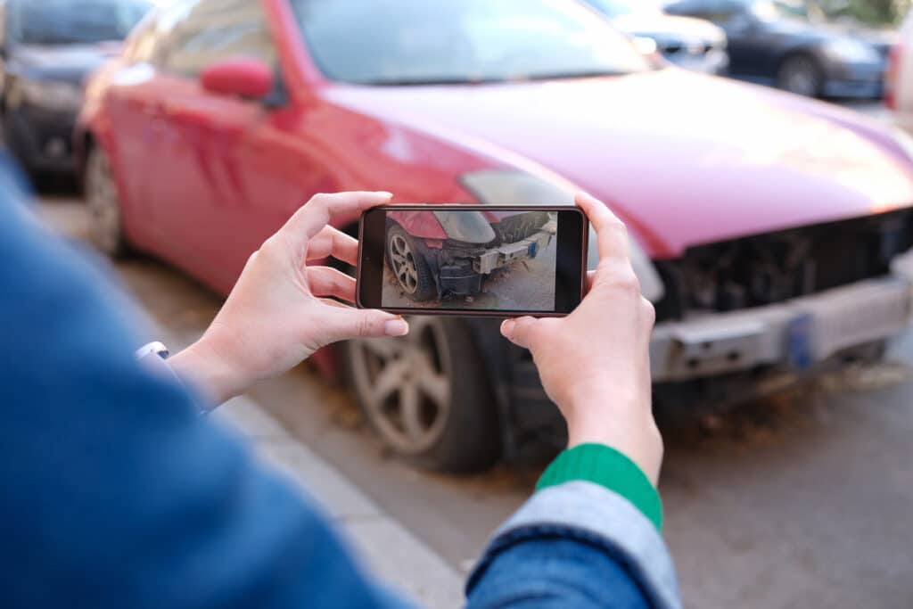 Close-up of woman insurance broker making photo of car after accident on smartphone. Damaged automobile and insurance case concept